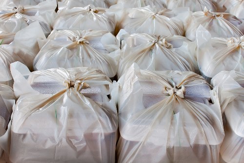A close-up image showing numerous tightly packed white plastic waste bags, each sealed with a knot at the top. The bags are arranged in rows, occupying the entirety of the frame, with some slight variations in shape due to the contents within. The plastic material appears to be glossy, reflecting light, and the bags contain various types of rubbish, likely household waste. They are situated outdoors on a concrete or paved surface, possibly on a driveway or pavement, suggesting a rubbish removal service preparing for collection. The background is blurred, emphasizing the uniformity and prominence of the waste bags, which are associated with rubbish clearance activities carried out by companies like South Kensington House Clearance to dispose of waste from residential or commercial properties in the South Kensington area or nearby postcodes. The image conveys an organized volume of waste ready for removal, aligned with professional rubbish clearance operations in London.